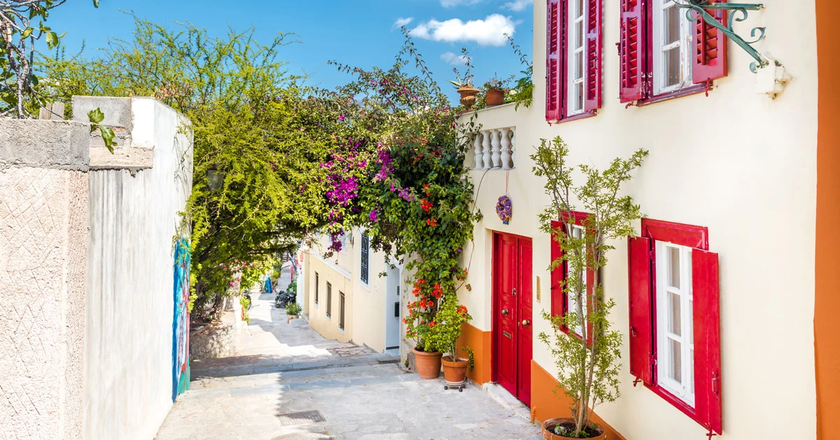 Where to Stay in Athens, Greece: small traditional houses with red windows and doors, surrounded by a huge blossomed bougainvillea, in Plaka, Athens.