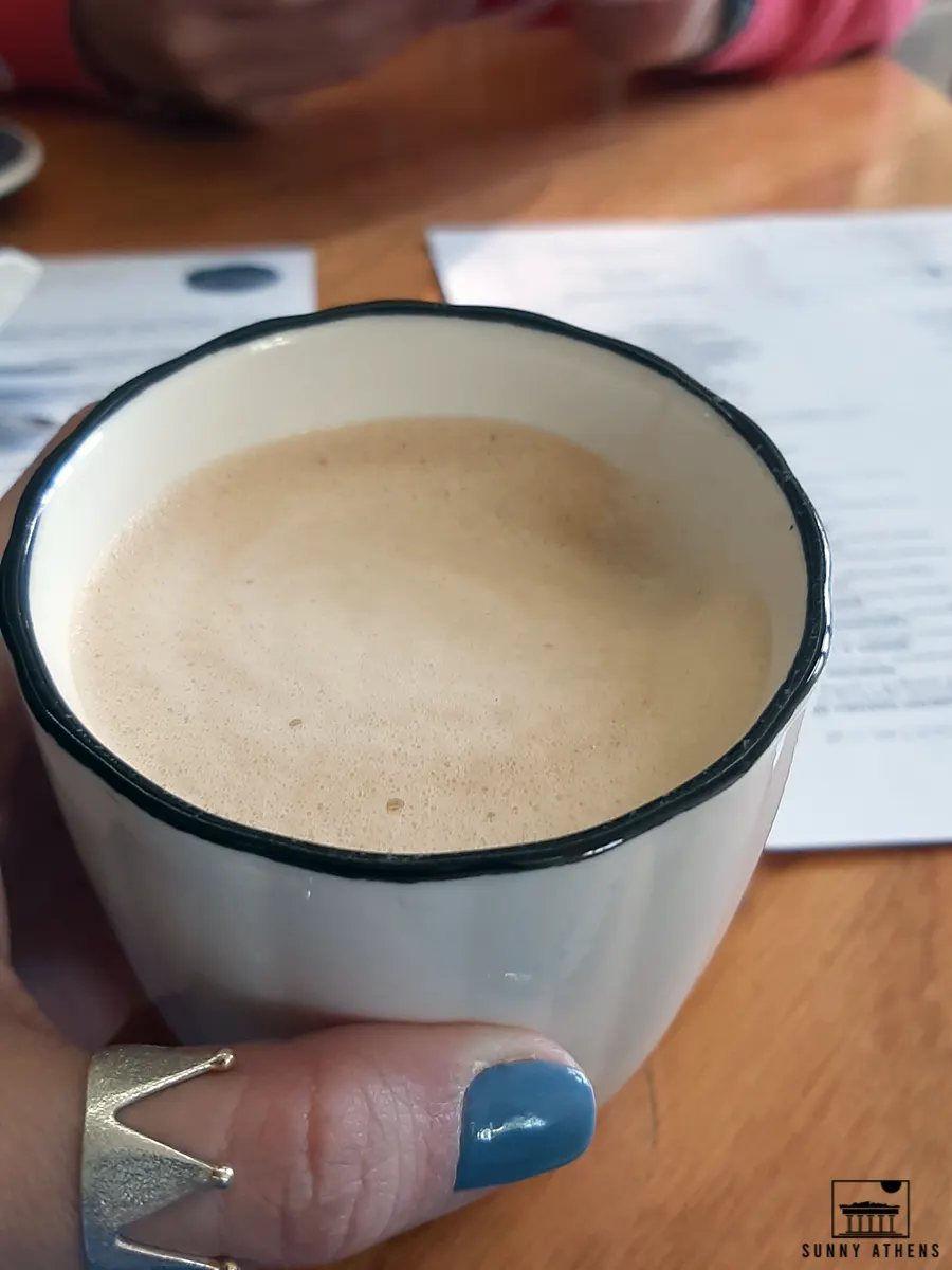 Chrysavgi holding a white cup with a specialty coffee with foam milk.