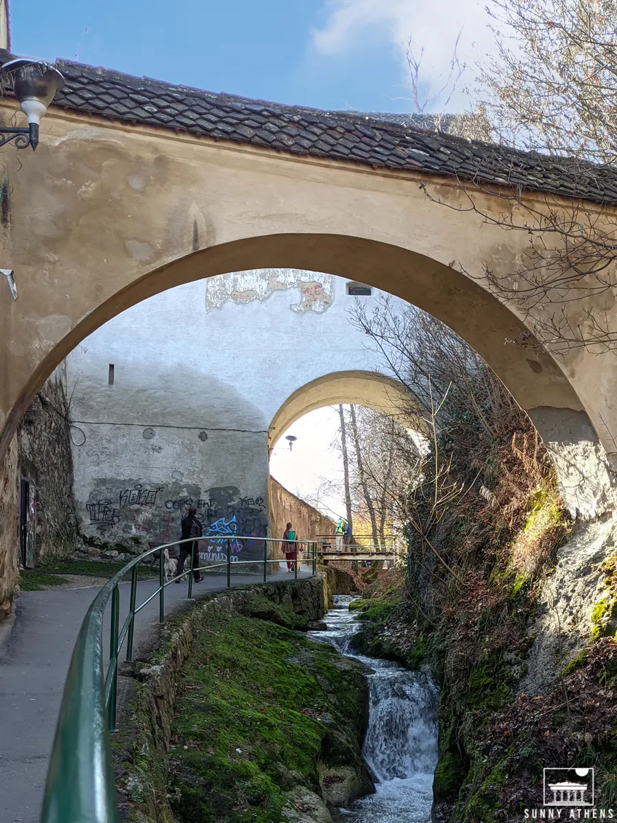 Two persons walking next to a creek near the Old Town of Brasov.