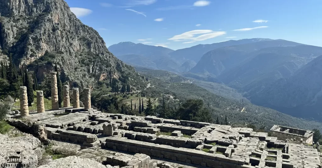 A panoramic view of ancient stone ruins at Delphi, set against a backdrop of rugged mountains and valleys.