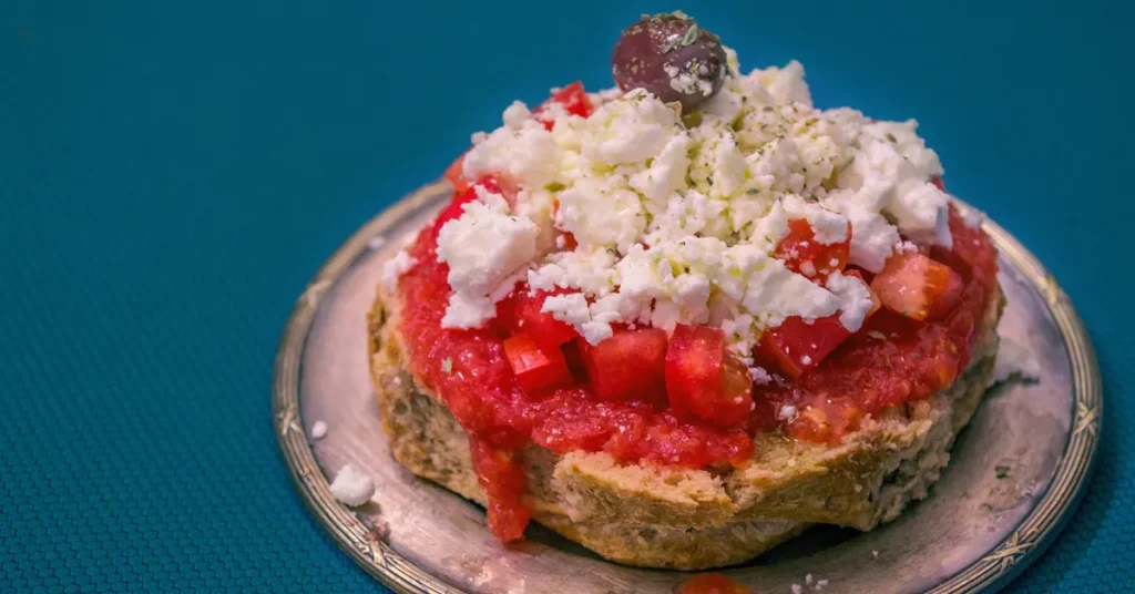 Traditional Greek dakos salad with chopped tomatoes and crumbled feta cheese on a crisp barley rusk, garnished with a single olive.