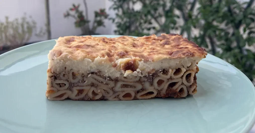 A slice of pastitsio, a Greek baked pasta dish with meat sauce, and creamy béchamel topping, served on a light blue plate.