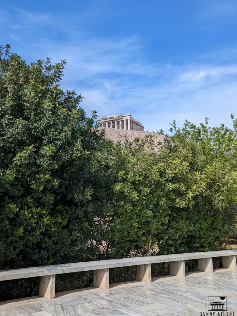 The Acropolis of Athens, under a clear blue sky, and a lot of trees in front of it.