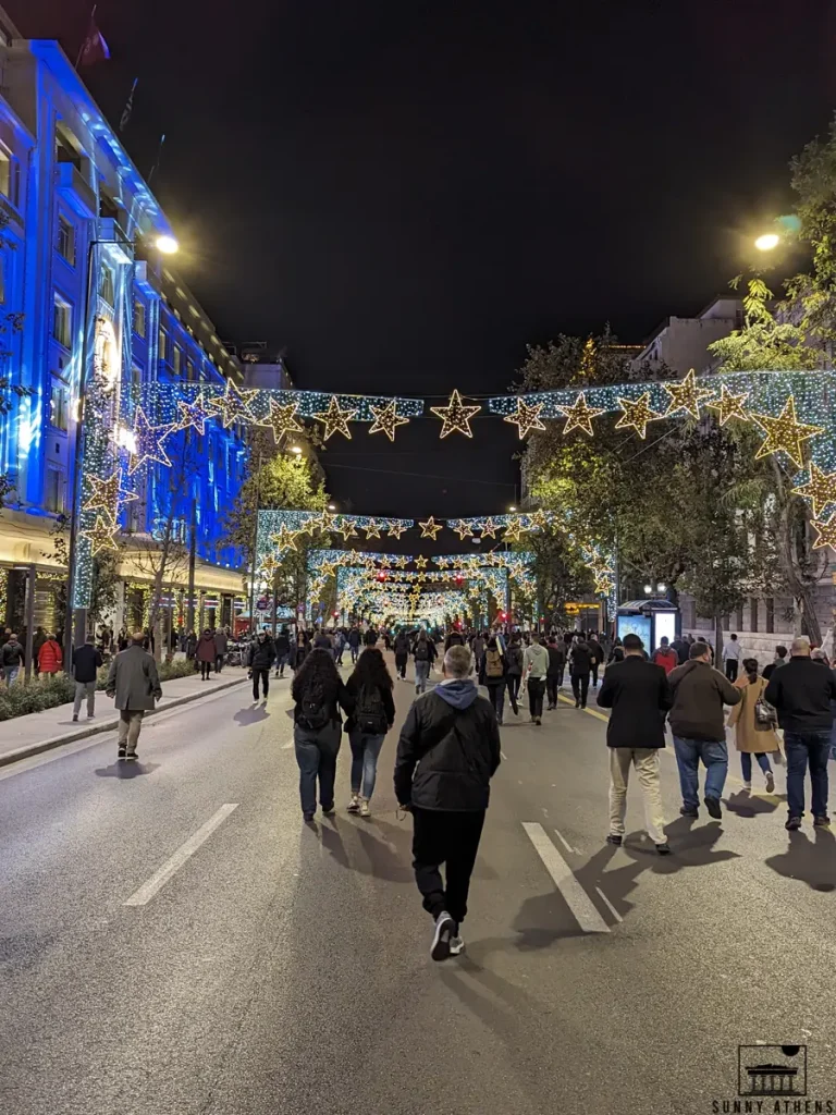 Stadiou Street in central Athens with holiday lights and stars, full of people during Christmas.