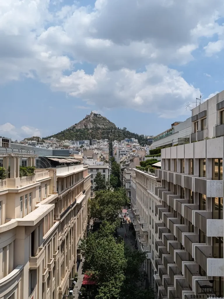 View of Lycabettus Hill, with trees in the foreground, as seen from Stadiou street, next to Syntagma.