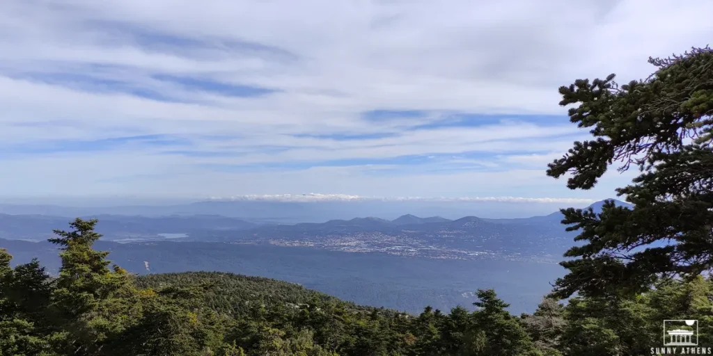 A scenic view from Mount Parnitha, with panoramic vista of Athens, and distant mountains under a sky with clouds.