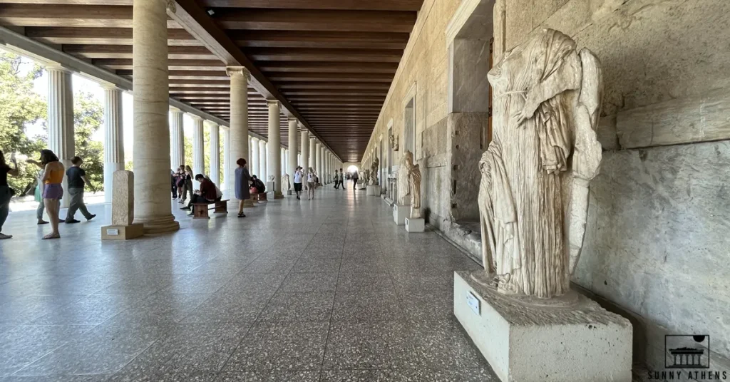 The Stoa of Attalos in the Ancient Agora of Athens, lined with marble statues and lot of visitors.