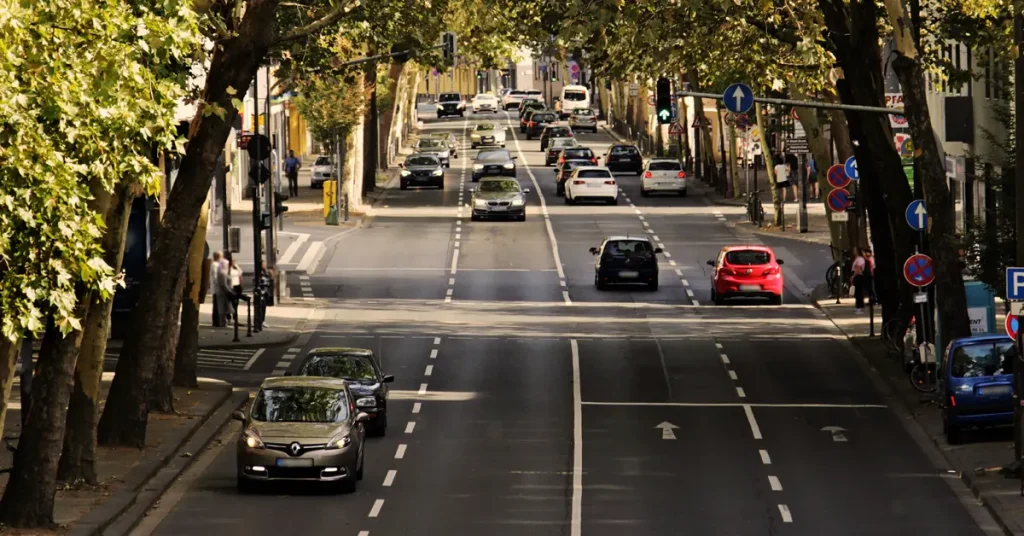 A dual carriageway with two lanes on each side, filled with cars and traffic lights visible in the background.