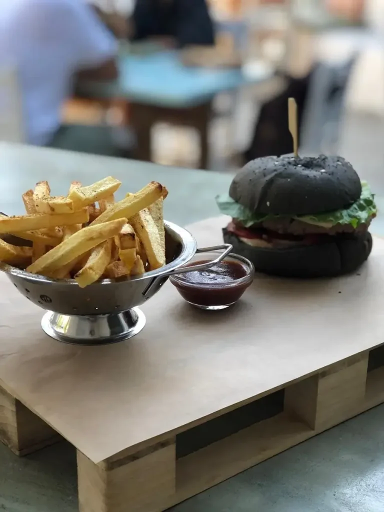 French fries, tomato ketchup, and a gourmet burger on black bread, served on a wooden plate at The Green Project.