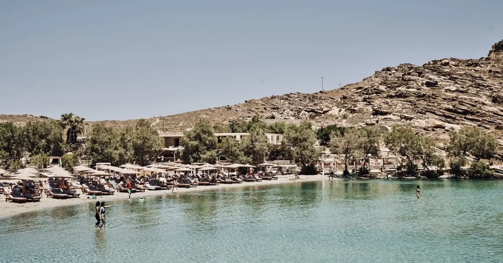 Monastiri Beach in Paros, Greece, lined with sunbeds shaded by umbrellas against a backdrop of rocky hills and crystal-clear waters.