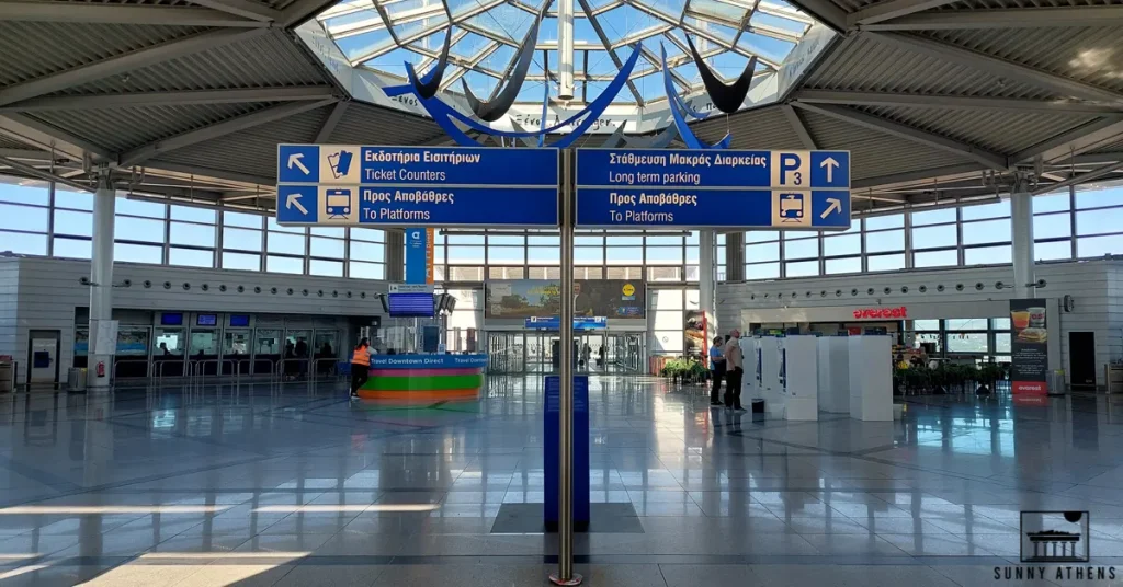 Blue signs with white letters pointing to the entrance of the metro and suburban railway at Athens International Airport.