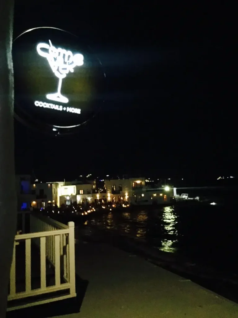 Paros Greece nightlife: A neon sign of a cocktail glass above the bustling Kosmos Bar.