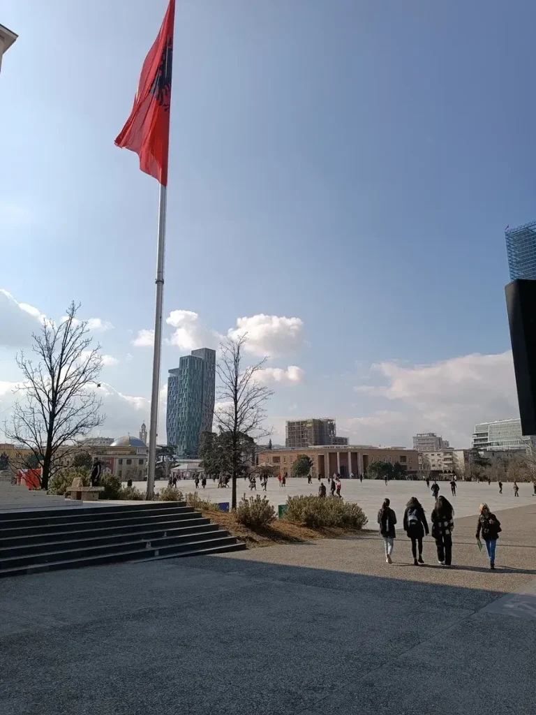 People walking next to an Albanian flag at Skanderbeg Square.