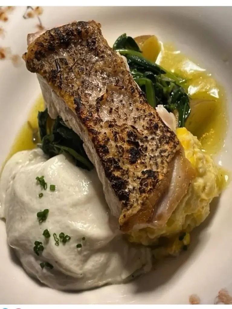 A roasted fish fillet served on a bed of greens and white sauce, from the menu of the Grande Dame restaurant.