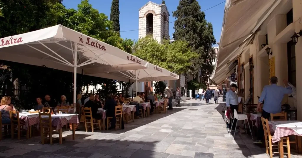 People dining outdoors under tents at Taverna Saita on a clear day, in Plaka, Athens.