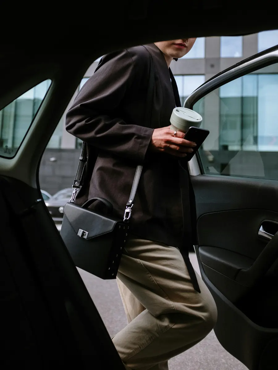 A person entering a taxi with a phone and coffee cup in hand.