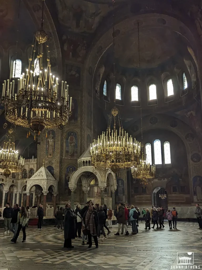 Interior of St. Alexander Nevsky Cathedral with chandeliers and people.