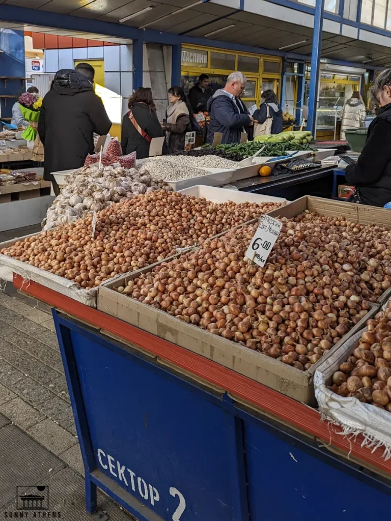 Outdoor market stall with piles of garlic and onions for sale.